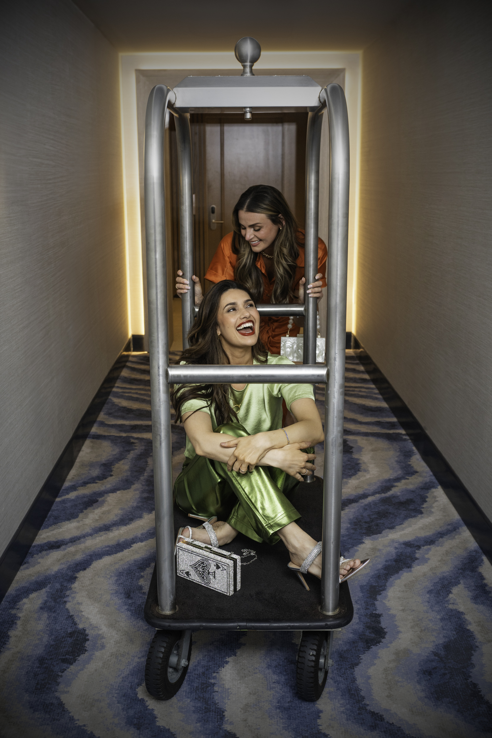 Friends celebrating a playful Friendsgiving getaway at Ocean Casino Resort, riding a luggage cart in the hotel hallway.