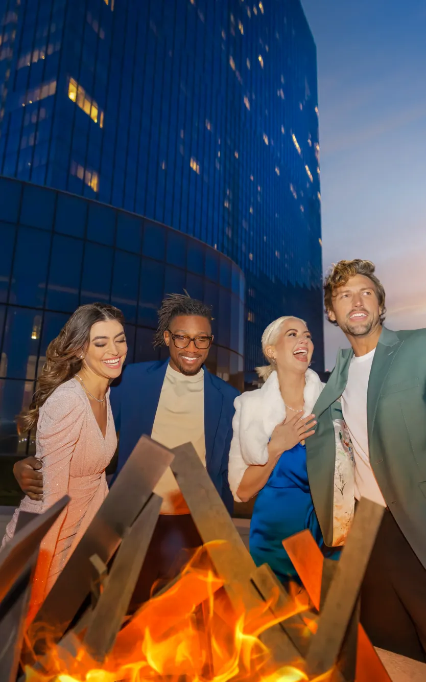 A group of friends laughing around a fire pit at the Park at Ocean Casino Resort