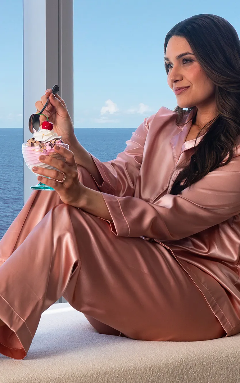 Image of a girl sitting in a suite overlooking the ocean, holding a cherry sundae