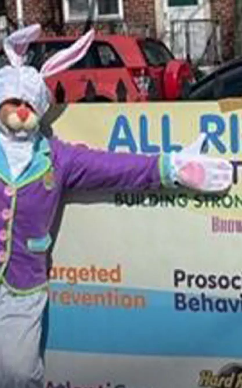 Someone dressed as an Easter bunny stands in front of a banner for an All Rise Event 