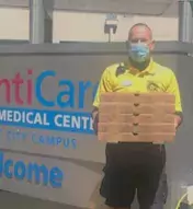 Man holding boxes of pizza stands in front of the sign for a medical facility