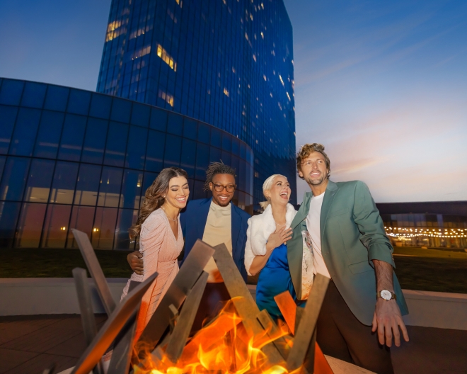 A group of friends laughing around a fire pit at the Park at Ocean Casino Resort